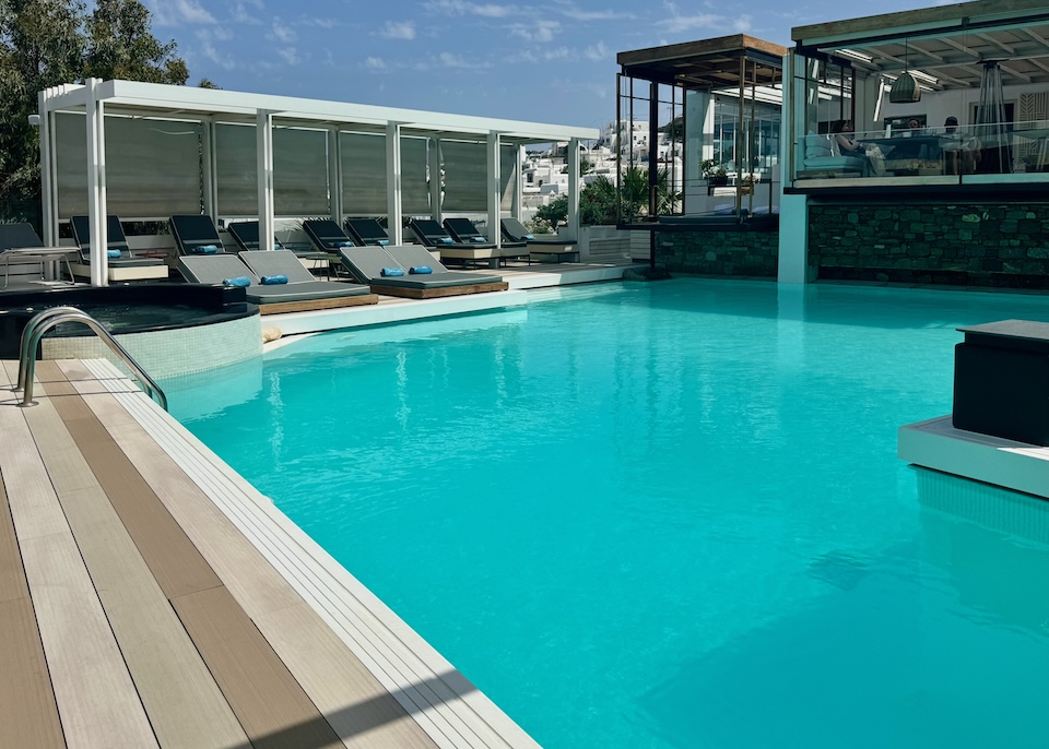 Single and double sunbeds on one side and a restaurant on the other side of a pool and jacuzzi at Semeli Hotel in Mykonos Town.