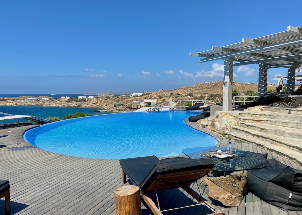 A kidney-shaped infinity pool with a wooden sun terrace overlooking the sea at Votsalaki near Paradise Beach in Mykonos.