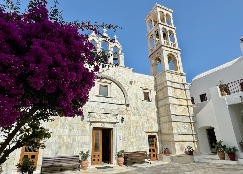 The marble façade and bell tower of a 16th-century church with a bougainvillea in front in Ano Mera, Mykonos.