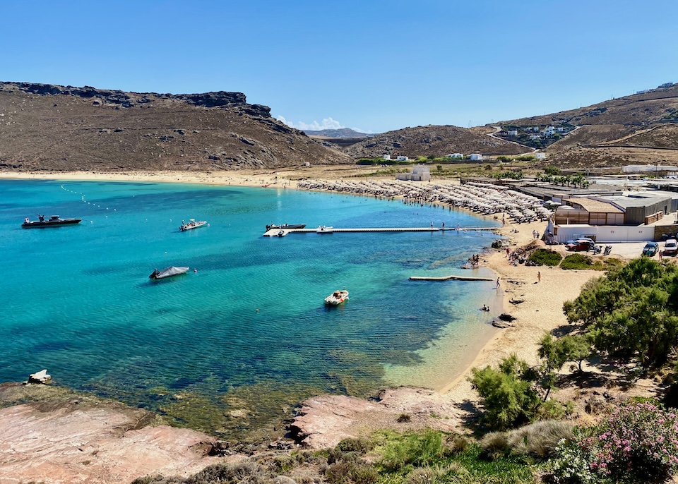 A few boats moored near a temporary pier in front of busy Panormos Beach in Mykonos.