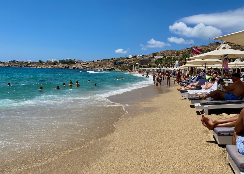 Golden sand and blue waves at a busy beach club on Paradise Beach in Mykonos.