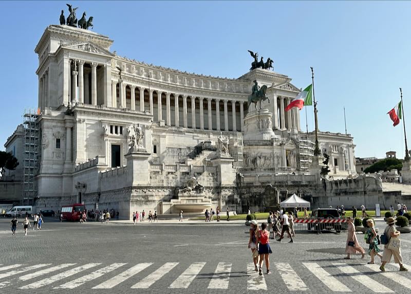 Large monument in a vehicular roundabout, with Italian flags flying