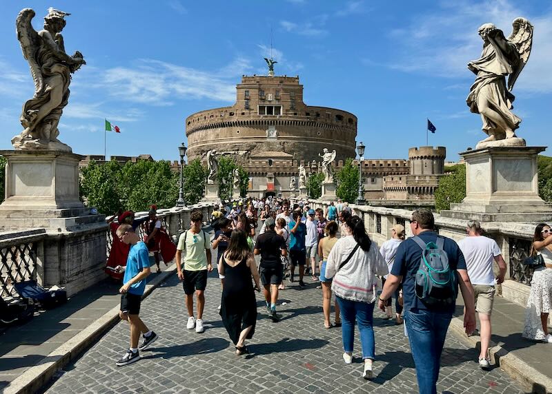 Tourists walk across a bridge toward a large circular stone castle