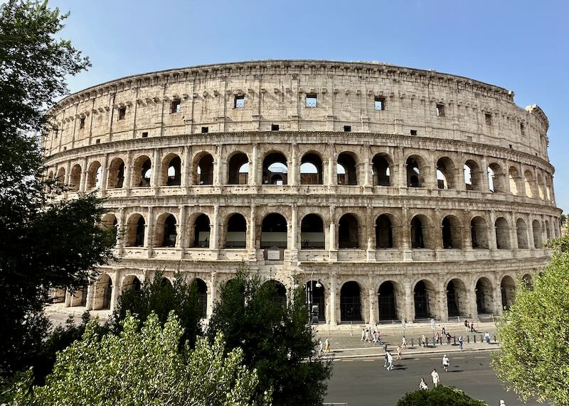 View of the Colosseum in Rome, seen through trees.