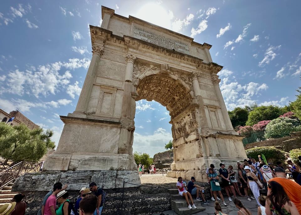 Looking up at a large stone archway at the Roman Forum on a sunny day.