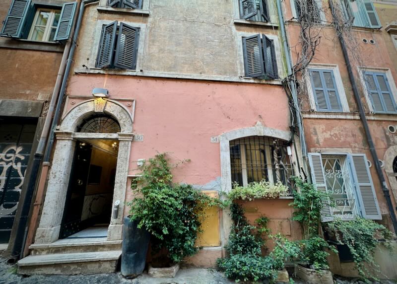 Arched stone doorway of a rustic pink building with potted plants in front