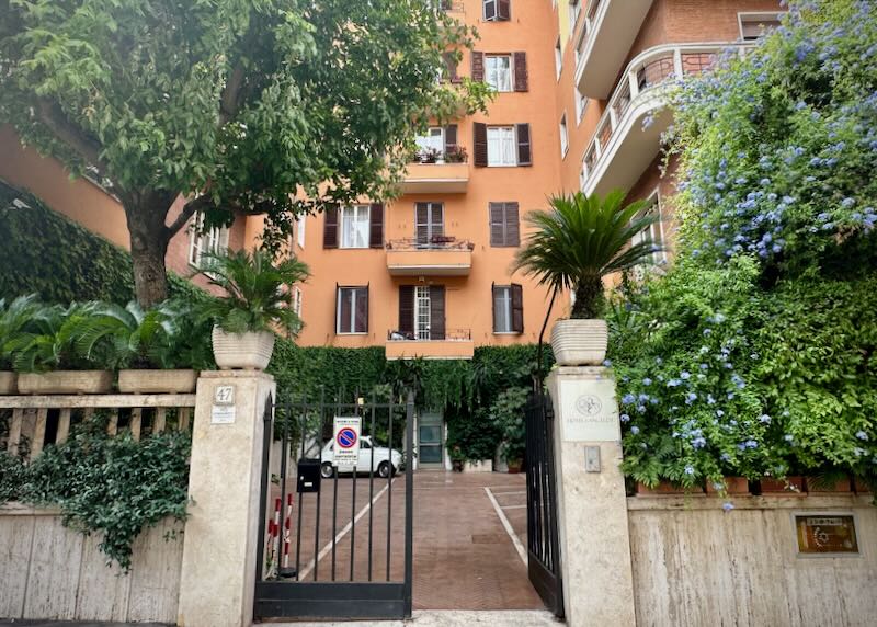 Open gate of a tangerine colored hotel building on a leafy street