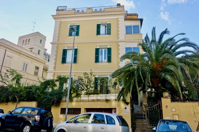 Small yellow hotel building on a residential street in Rome with a car parked in front