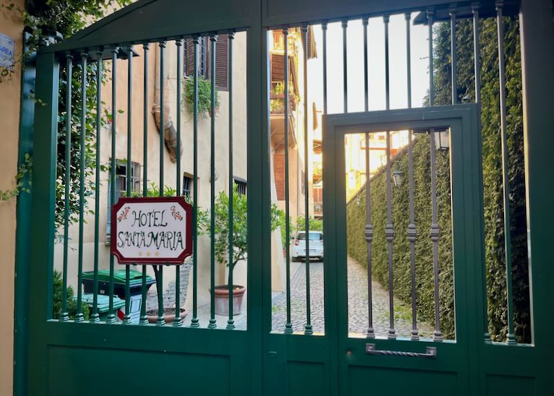 View looking through locked gates to a rustic hotel property with potted plants