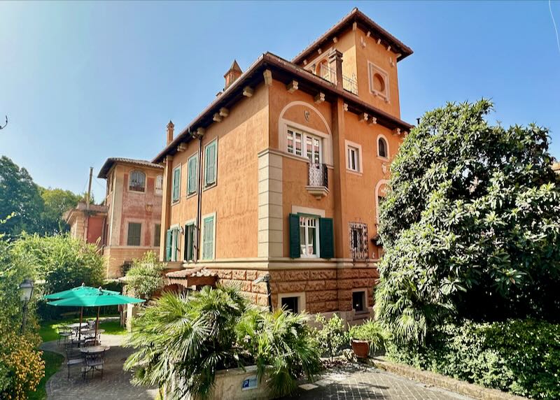 Stately Roman guesthouse with unbrella-covered tables in a shaded courtyard