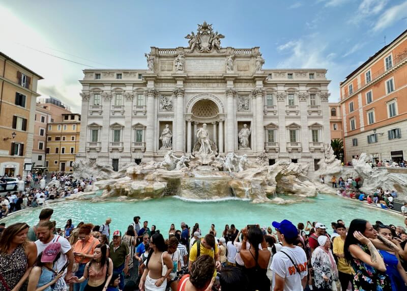 Crowds of tourists taking photos at the Trevi fountain in Rome.