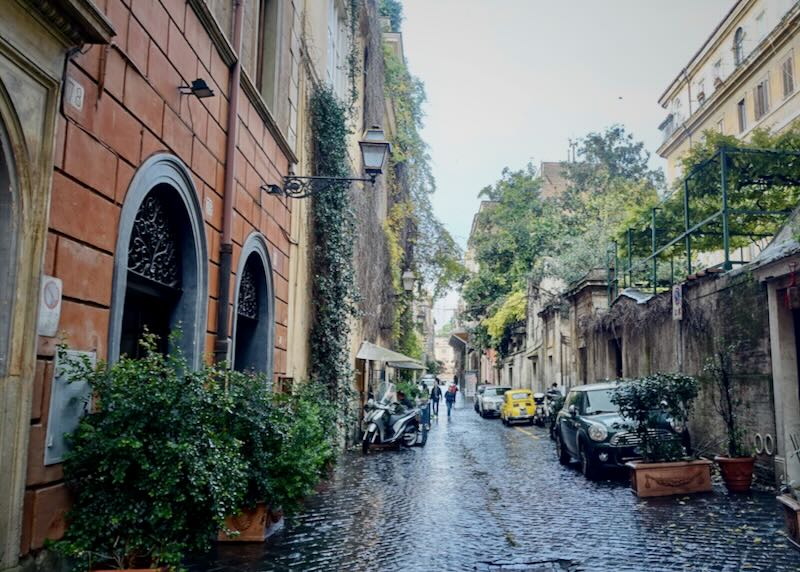 A narrow cobbled street lined with colorful stone buildings and potted plants