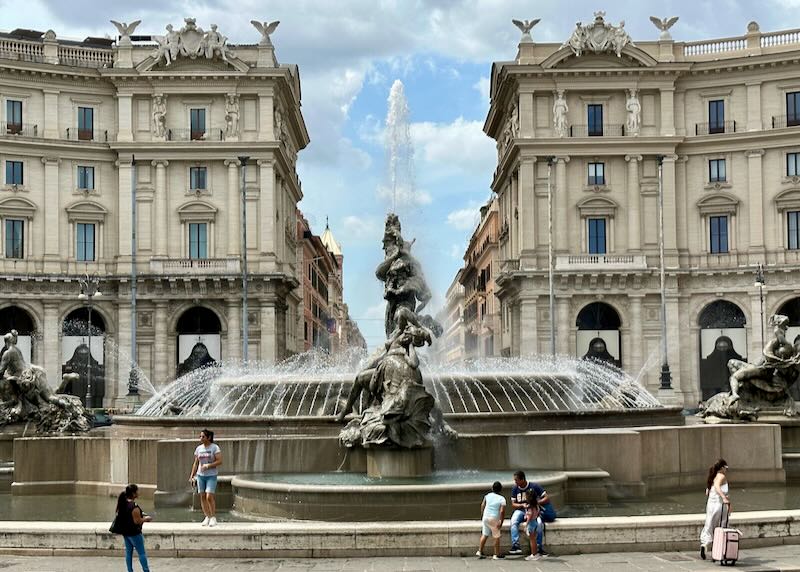 Large decorative water fountain with tourists resting at the base