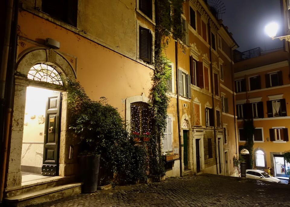 Light spills from the doorway of a hotel on a rustic Italian street at night