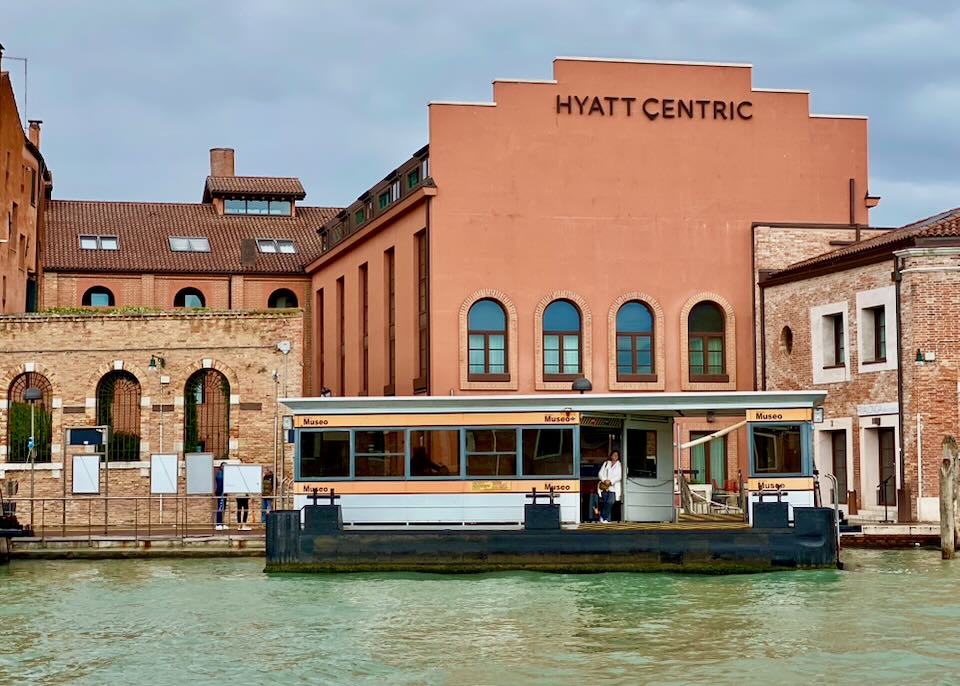 A woman waits at a waterbus stop in front of a modern hotel in Venice