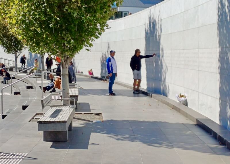 Visitors point to names on a memorial wall.