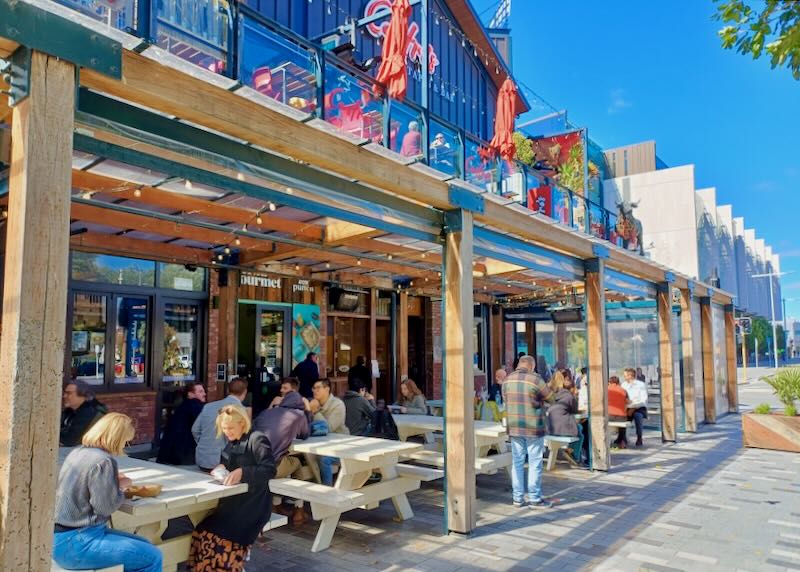 People sit outside on picnic tables at a market.