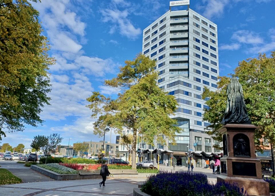 A person walks through a park by a tall hotel.