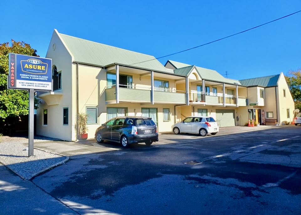 A yellow two-level motel has cars parked in front.