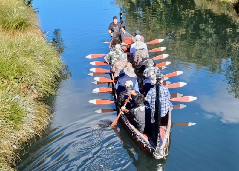 A wooden boat full of guests hold red paddles.