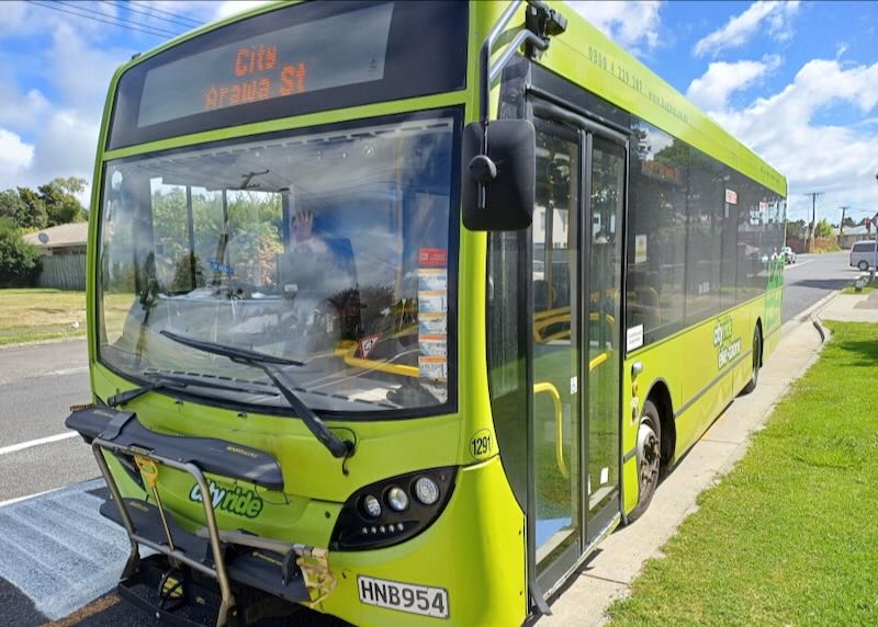 A lime-green bus sits on the side of the road at a bus stop.