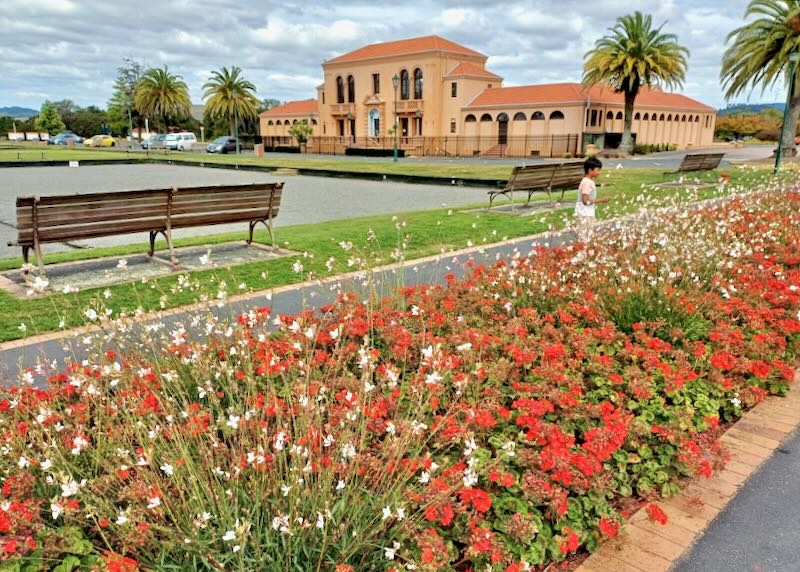 A patch of red flowers line a sidewalk to a terracotta-colored building.