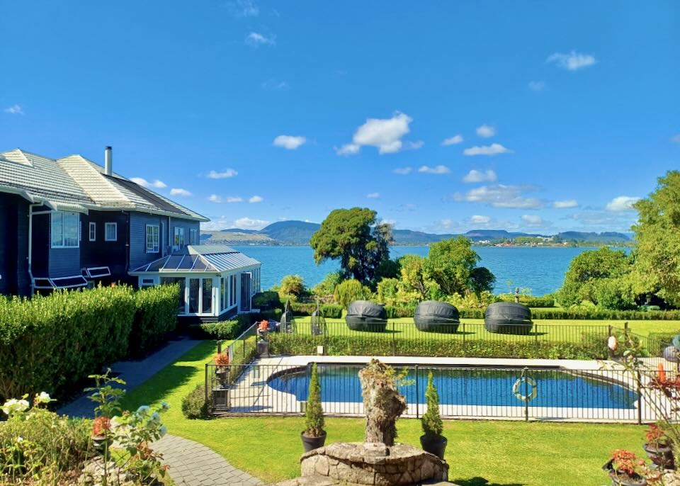 A blue outdoor pool sits on green lawns by a blue lake.