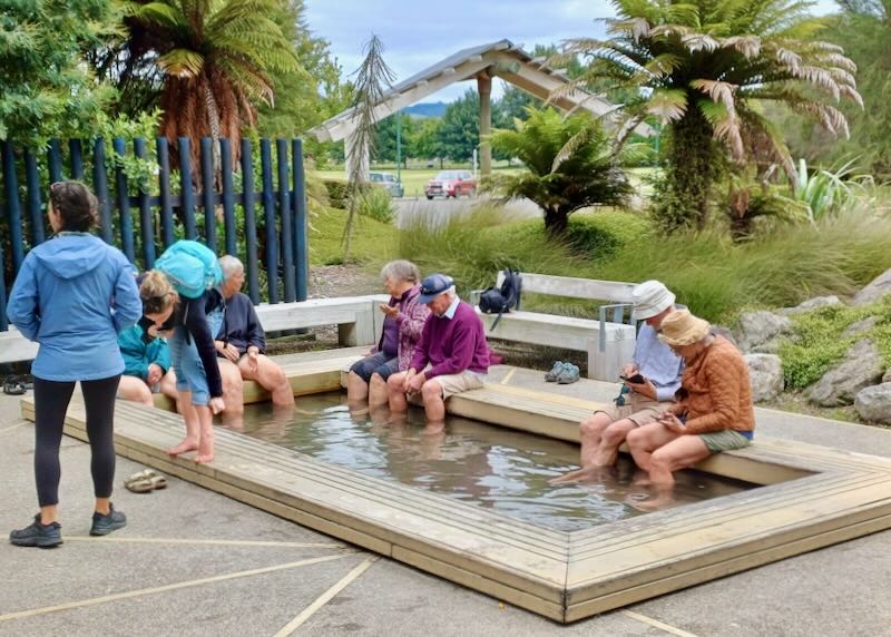 A group of people sit with their feet in mineral spring water at a park.