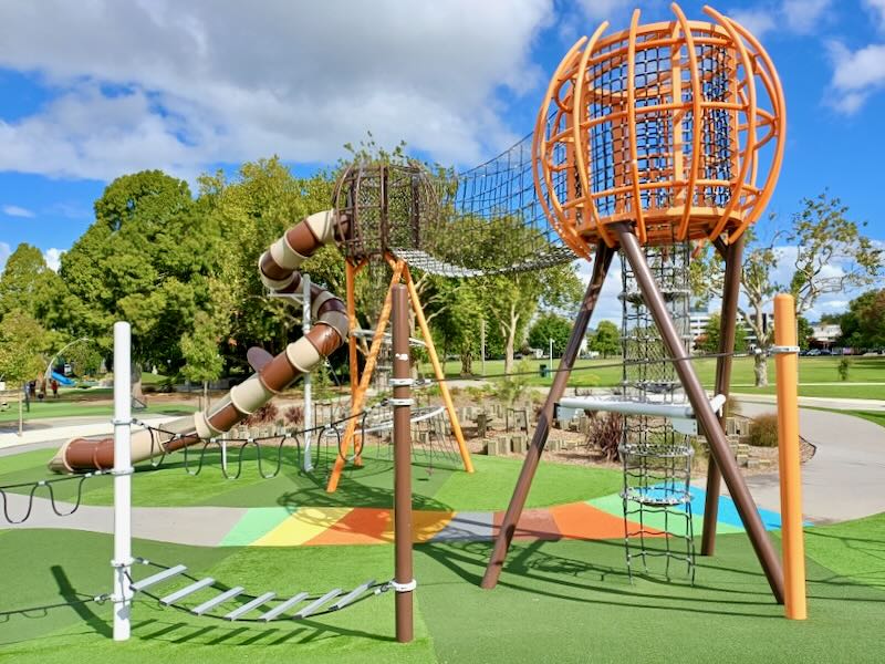 A colorful outdoor children's park with green astro-turf, a slide, and jungle gym.