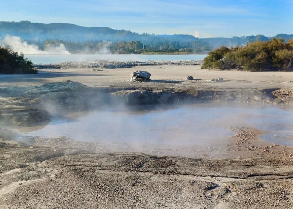 Ponds of shallow steaming water and mud bubble by the side of a dirt road.