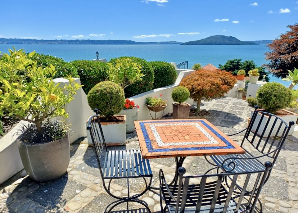 A table and chairs sit in front of a stone fence overlooking a lake and green island in the distance.