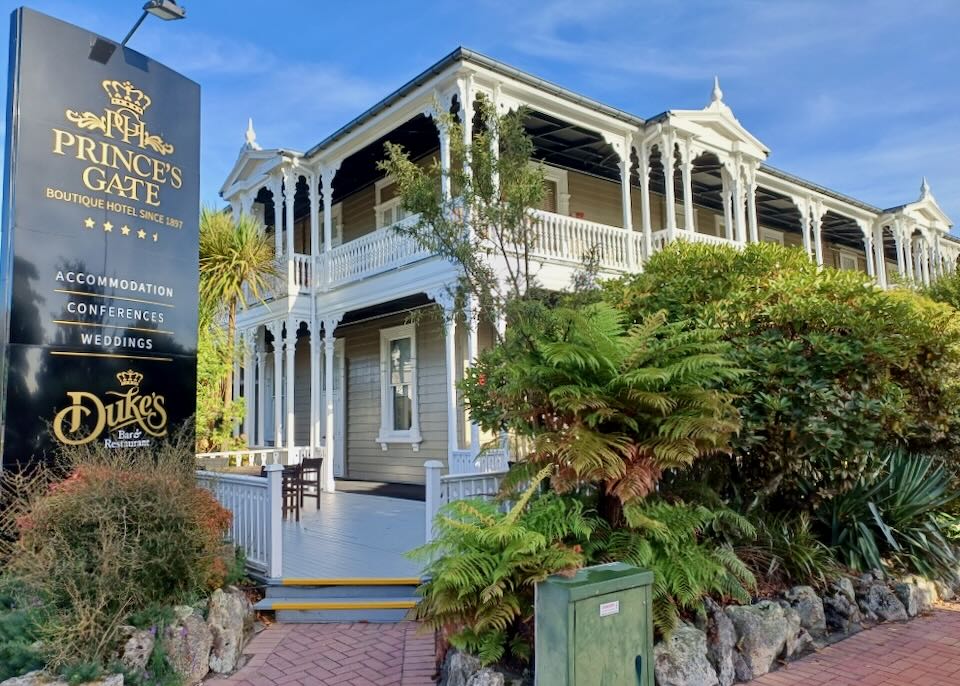 A tan colonial style building with a white wrap-around wood porch.