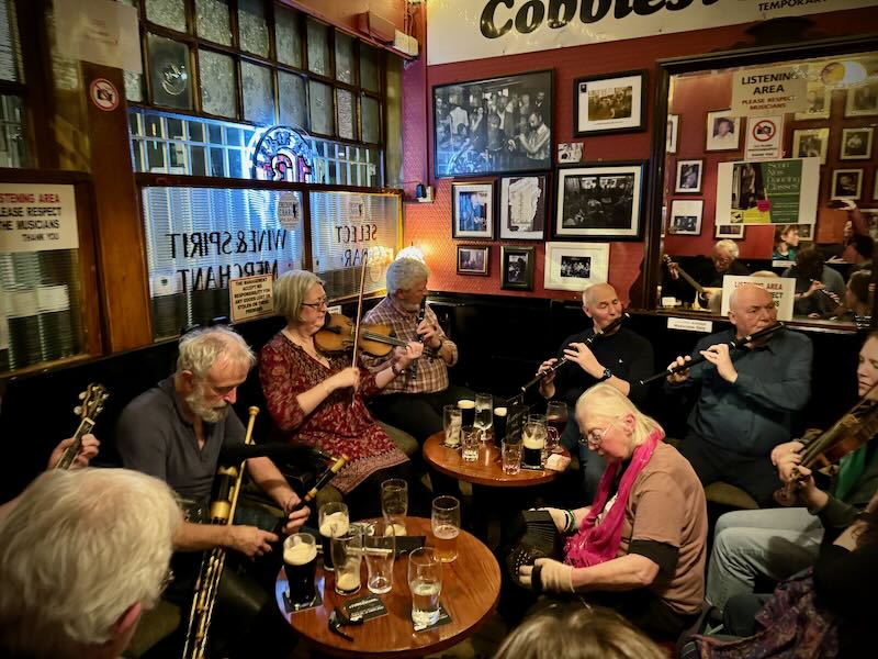 Musicians playing instruments around pub tables crowded with pints of beer 