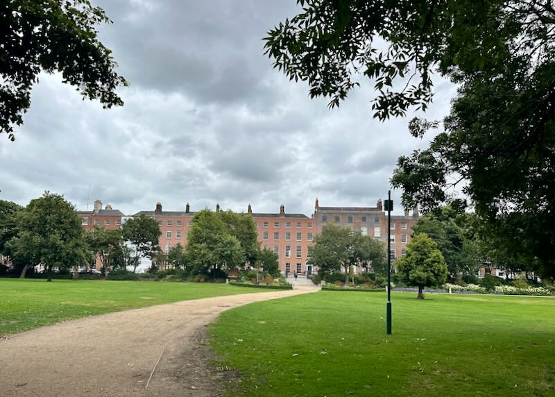 Green park expanse with a gravel path leading to a row of townhouses