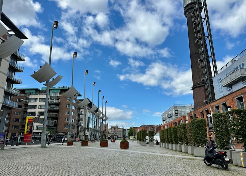 Pedestrian plaza lined with industrial buildings and modern sculpture