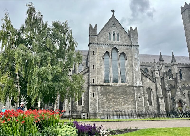 Side view of St Patrick's Cathedral across a green lawn with flowering landscaping