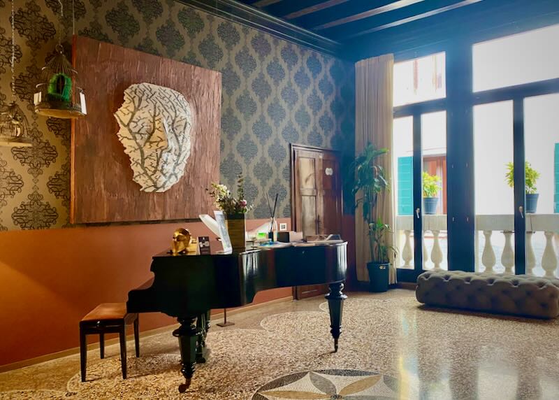 A grand piano on a terrazzo tiled floor in a room with the light streaming in through large windows