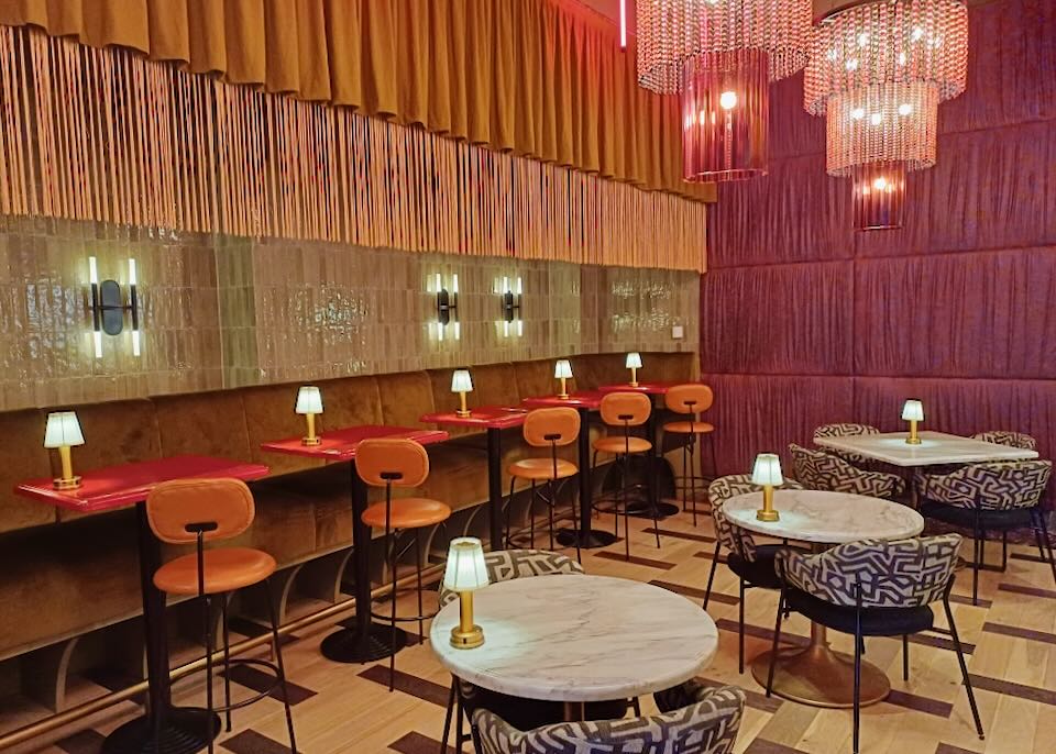 Bight pink velvet fabric walls next to a tiered orange ruffled and fringed wall with a long booth.