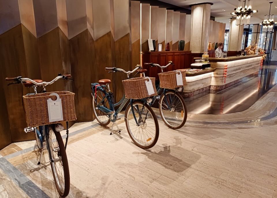 Cruise bikes with dark blue frames and wicker front baskets sit in a warm-colored lobby.