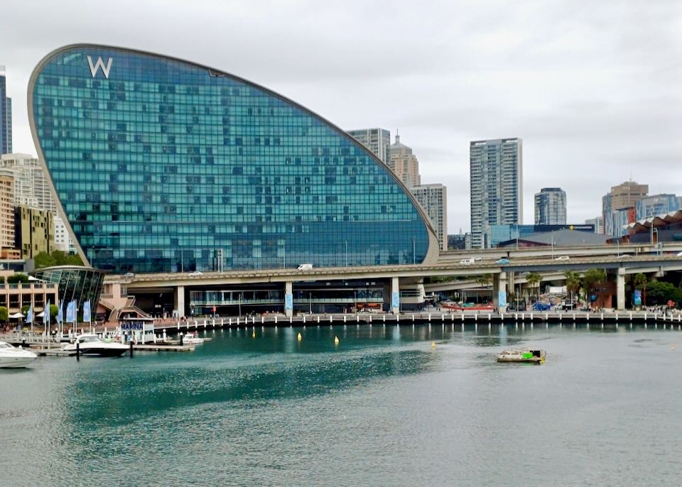 A tall curved hotel with blue windows overlooks a harbor.