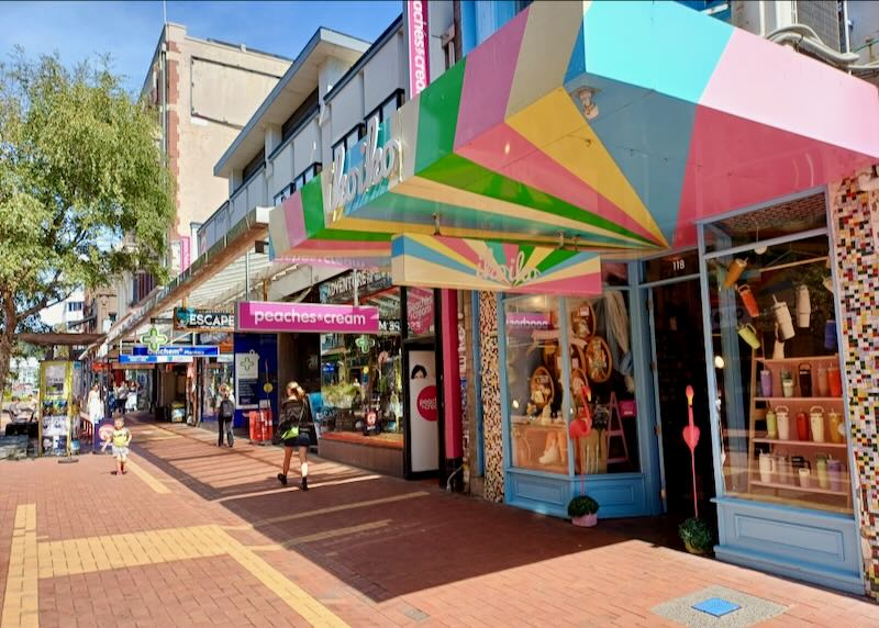 People walk on a sidewalk next to colorful unique stores.