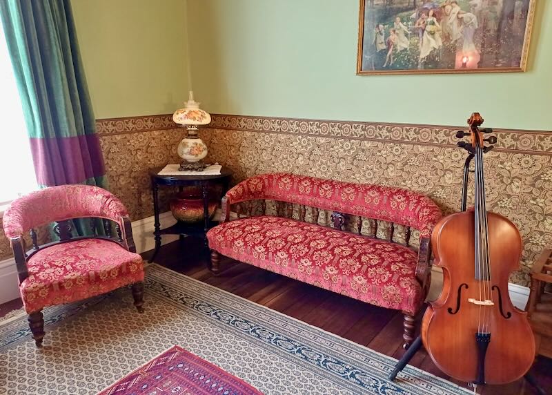 A red floral-print sofa and chair sit in a living room next to a cello.