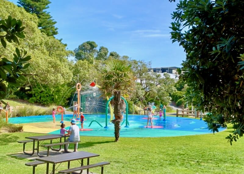 Kids run through colorful water fountains at a park.