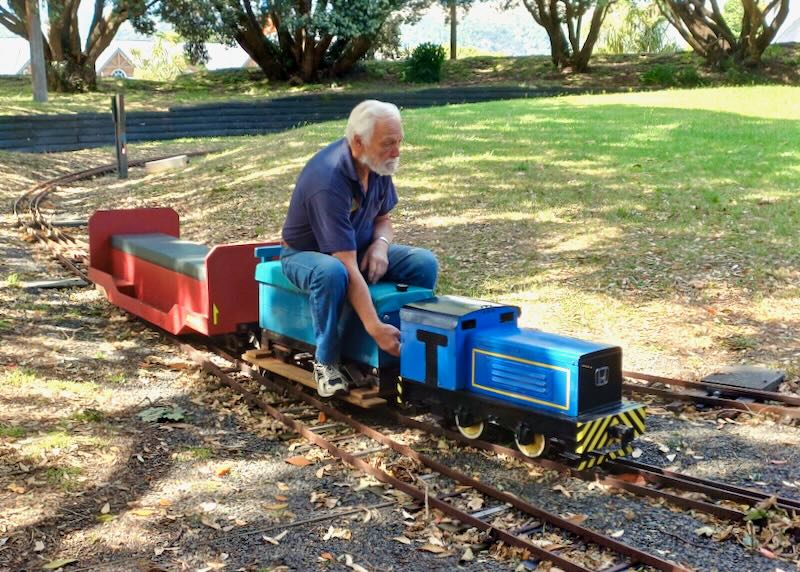 A man sits on a small train meant for kids.