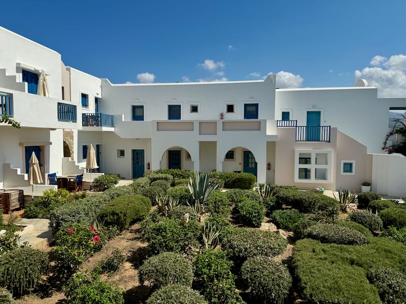 Boxy white exterior of a Greek hotel, with landscaped gardens in center.