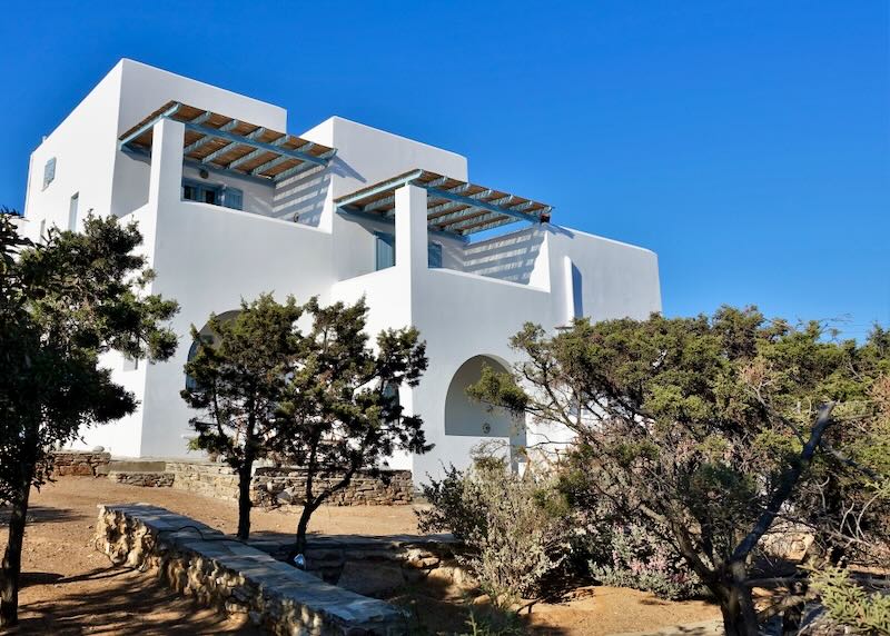 Whitewashed, cubic exterior of Oliaros Seaside Lodge surrounded by trees in Antiparos.