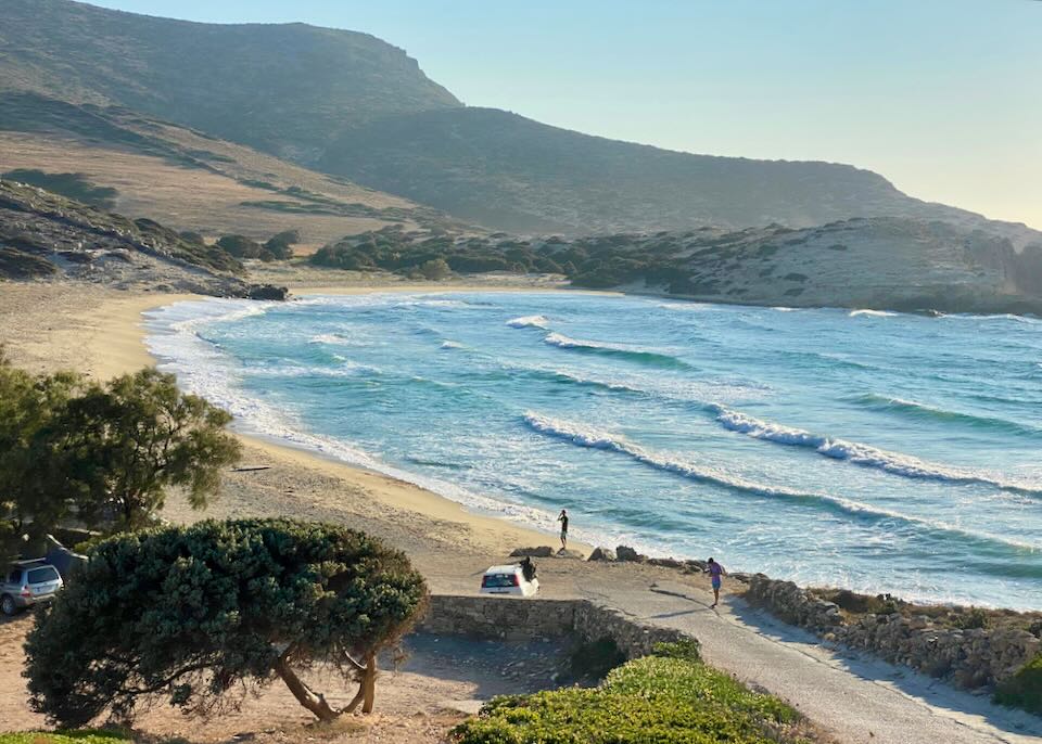 Beach in late afternoon, with blue waves rolling in and green hills in the background.