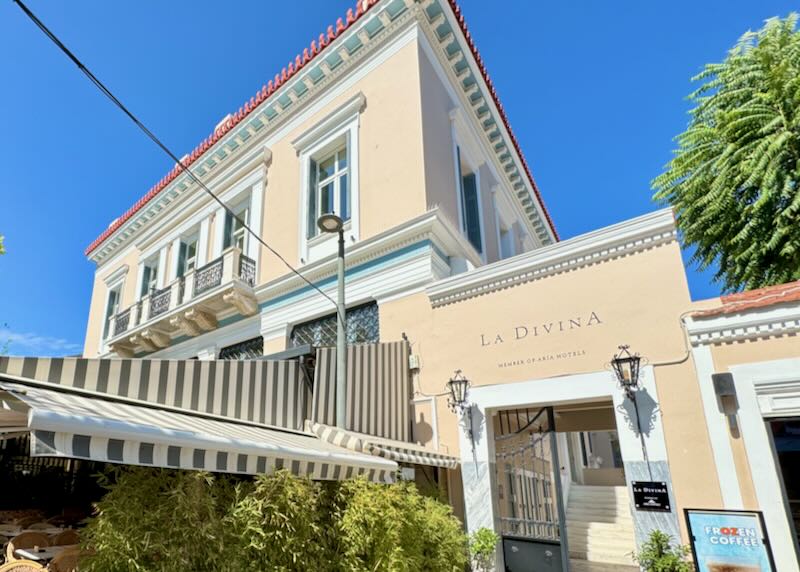 Exterior of a peach-colored Mediterranean-style hotel with clay tile roof and striped awning on a sunny day 