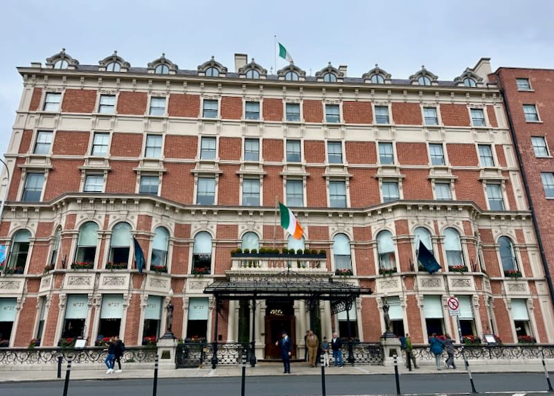 Front view of an ornate red brick hotel with an Irish flad flying in front.