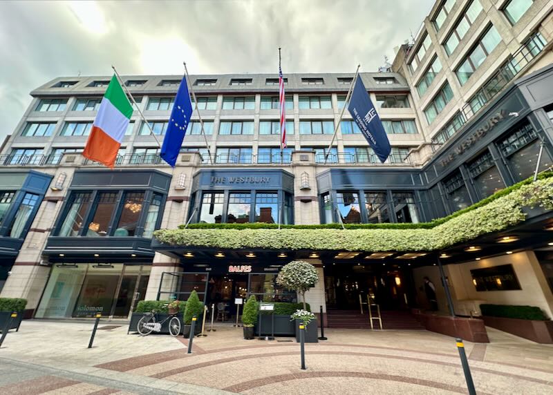 View looking up at the awning-covered entrance of a hotel with flags hanging above. 